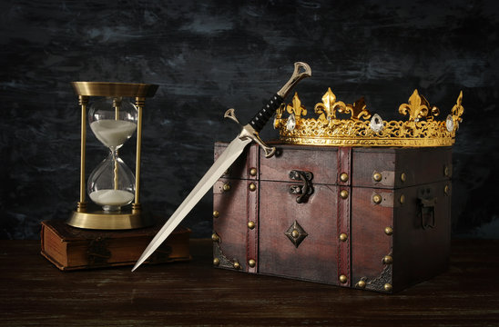 low key image of beautiful queen/king crown, vintage hourglass and sword. fantasy medieval period.