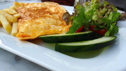 Omelette in a plate side view. Closeup omelette with cherry tomatoes, salad, cucumber and french fries. 