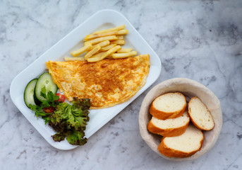  Omelette in a plate on marble background, top view. Omelette with cherry tomatoes, salad, cucumber and french fries. Flat lay breakfast with omelette, vegetables and bread basket. 