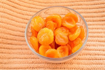 Dried apricots in glass bowl on orange textile background. Healthy food and fruits