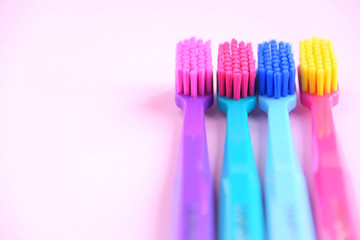 Colorful toothbrushes with selective focus on pink background. Toothbrush for personal routine morning  hygiene on neutral blurred backdrop. Dental plastic tool with empty space for image or text