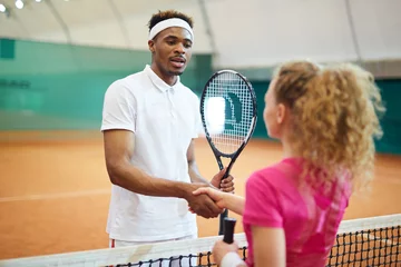 Fototapeten Young African-american man in activewear shaking hand of his playmate over net on the court © pressmaster