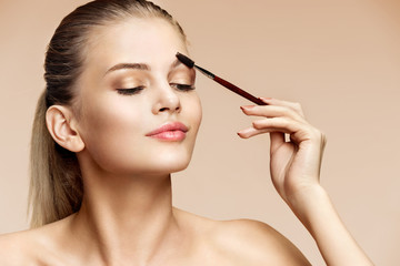 Beautiful woman using brush for brows. Photo of attractive woman with perfect makeup on beige...