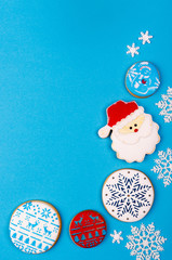 Christmas background on blue paper with biscuits, gifts and snowflakes. Painted Christmas cookies and gingerbread. Vertical composition with copy space.