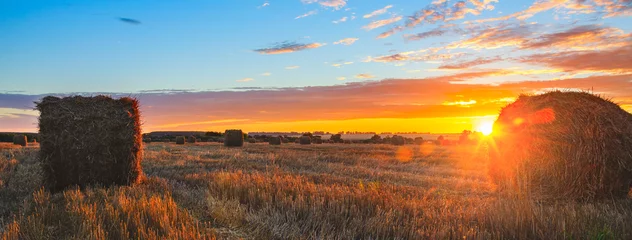 Photo sur Plexiglas Été Vue panoramique des balles de foin sur le terrain après la récolte éclairée par les derniers rayons du soleil couchant