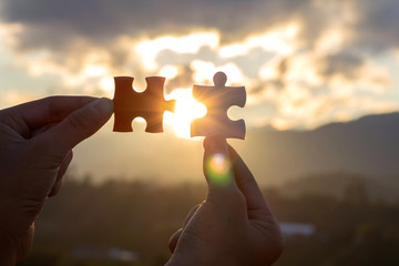 hands holding piece of jigsaw puzzle and sunset background. teamwork concept