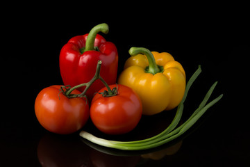 Fresh, appetizing vegetables lie on a dark reflective surface on a black background.