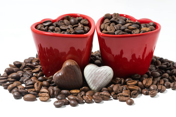 red cups with coffee beans and chocolate candies in the form of heart, closeup