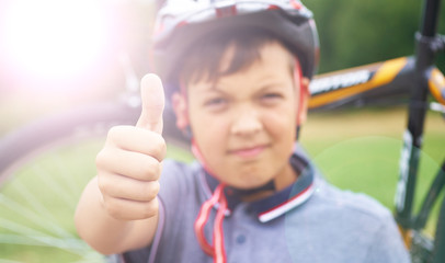 Riding is super. Portrait of smiling teenager riding bike and giving thumbs up on background of park and bike.