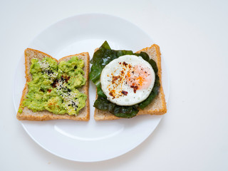 Appetizing bruschetta with egg and avocado on a plate. On the Sandwich, the avocado pulp and fried quail egg. Dark background. View from above. Close-up. Macro photography.