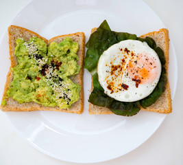 Appetizing bruschetta with egg and avocado on a plate. On the Sandwich, the avocado pulp and fried quail egg. Dark background. View from above. Close-up. Macro photography.