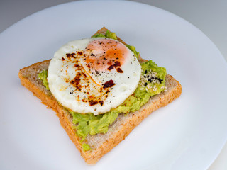 Appetizing bruschetta with egg and avocado on a plate. On the Sandwich, the avocado pulp and fried quail egg. Dark background. View from above. Close-up. Macro photography.