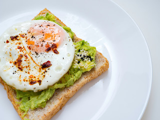Appetizing bruschetta with egg and avocado on a plate. On the Sandwich, the avocado pulp and fried quail egg. Dark background. View from above. Close-up. Macro photography.