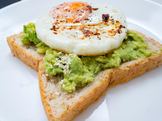 Appetizing bruschetta with egg and avocado on a plate. On the Sandwich, the avocado pulp and fried quail egg. Dark background. View from above. Close-up. Macro photography.