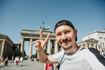 Tourist guy makes selfie on the background of the Brandenburg Gate in Berlin in Germany and shows...