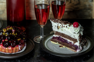 sweet meal for two: red wine, cake with icing and fruits, chocolate cake with cherry and whipped cream