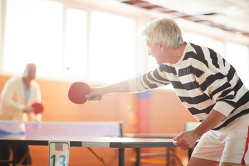 One of ping pong players hitting ball while passing it over table to his mate during game in the hall