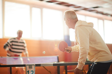 One of active men hitting ping pong ball over table while enjoying game with his friend in sports...