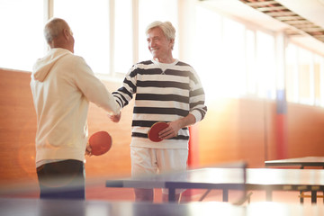 Two senior ping pong players shaking hands after or before game while standing by table