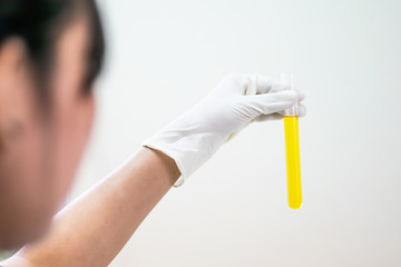 Color liquid in test tube hold in hand with glove of scientist isolated on the light plain wall