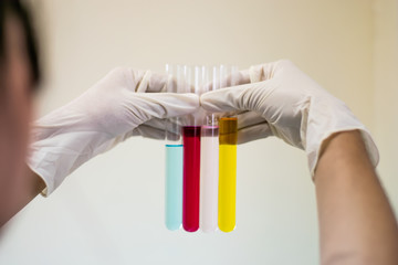 Color liquid in test tube hold in hand with glove of scientist isolated on the light plain wall