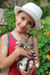 Little smiling boy in a hat staying with striped cat on his hands closeup