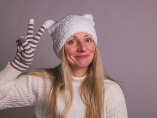 Obraz premium happy adult woman in funny kids hat with ears showing the sign of victory, hand in striped gloves