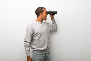 African american man on white wall background and looking for something in the distance with binoculars
