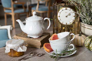 Still life. White beautiful teapot, cups and saucer, apricot jam, grapefruit and rosemary. Against the backdrop of vintage watches and heather.