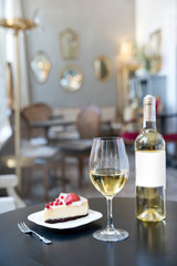 A bottle of white wine, a glass and a cake on the background of a vintage cafe