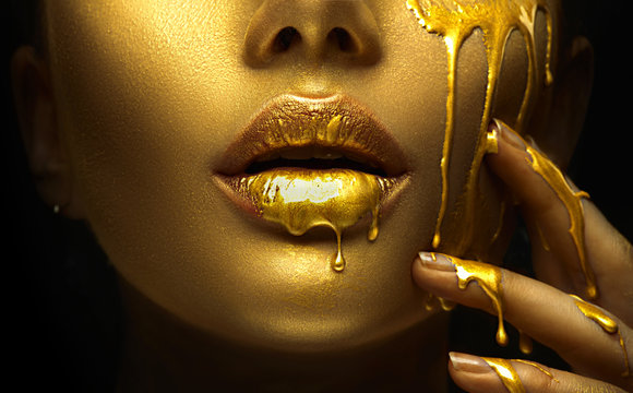 Fototapeta Golden paint smudges drips from the face lips and hand, golden liquid drops on beautiful model girl's mouth, creative abstract makeup. Beauty woman face