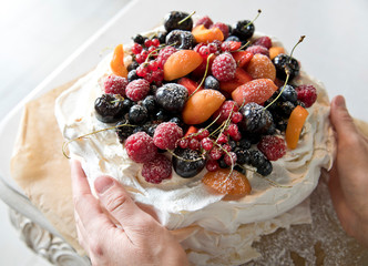meringue cake with berries and fruits. Hands holding a cake