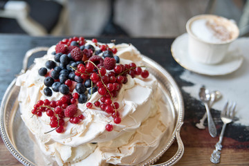 Meringue cake with berries on a silver tray and a cup of coffee