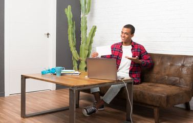 African american man with laptop in the living room holding an empty white placard for insert a concept