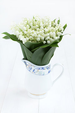Beautiful bouquet of lilies of the valley in jug on white painted wooden table