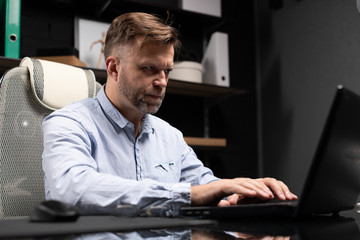 Fototapeta premium Serious businessman typing on laptop in stylish, modern office