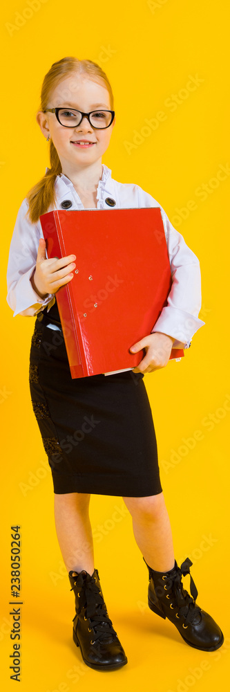 Wall mural Girl with red hair on a yellow background. A charming girl in transparent glasses is holding a large red folder in her hands.