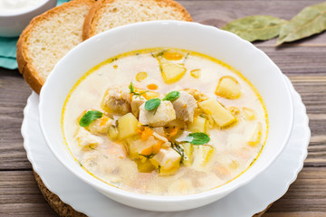 Fresh chicken broth soup with potatoes and herbs in a white bowl on a wooden table