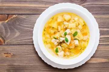 Fresh chicken broth soup with potatoes and herbs in a white bowl on a wooden table. Top view