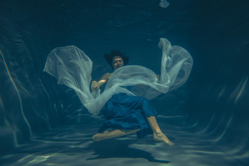 elegant pretty woman swims underwater like a free diver in a blue evening dress alone