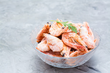 Group of frozen shrimp and a leaf of arugula in a glass bowl on a gray table