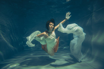 elegant slender girl swims underwater like a free diver in a white evening dress with beautiful fabric