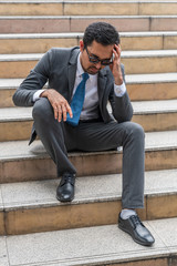 Fototapeta na wymiar A sad looking young businessman sitting at the staircase looking down with stressed and depressed look gesture