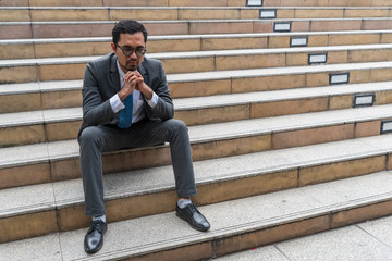 A sad looking young businessman sitting at the staircase looking down with stressed and depressed look gesture