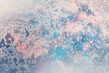 Winter background in soft pastel colors. Frost and snowflakes on the window. Multicolored bokeh with blur. Glare through glass. Background for holiday greetings with winter theme.