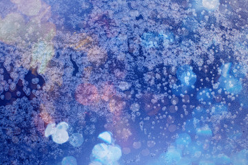 Winter background in soft pastel colors. Frost and snowflakes on the window. Multicolored bokeh...