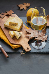 A glass of white wine served with cheese in a cutting board on dark background