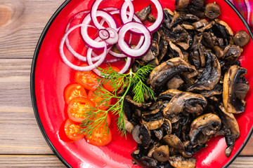 Ready-to-eat appetizer - fried mushrooms, cherry tomatoes and onions on a plate on a wooden table. Top view