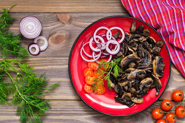 Fried mushrooms, onion and cherry tomatoes on a plate on a wooden table. Rustic style. Top view