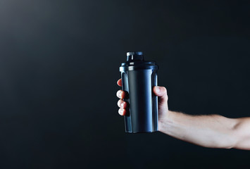 Arm of a muscular sportman  with a black shaker on a dark background.